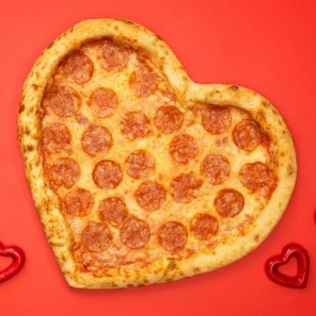 Pizza pepperoni w kształcie serca na walentynki na czerwonym tle papieru