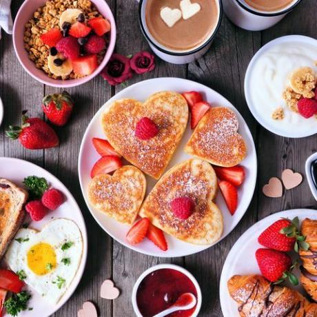 scena stołu śniadaniowego walentynki lub matki na ciemnym drewnianym tle z naleśnikami w kształcie serca, jajkami i jedzeniem o tematyce miłości