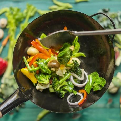smaż i smaż różne świeże, kolorowe warzywa rynkowe w gorącym, parującym woku z warzywami na turkusowym drewnianym stole pod wokiem